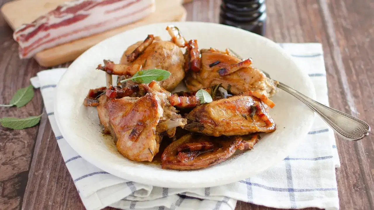 Delizioso coniglio in padella, dorato e succulento, guarnito con pancetta croccante e foglie di salvia fresca.