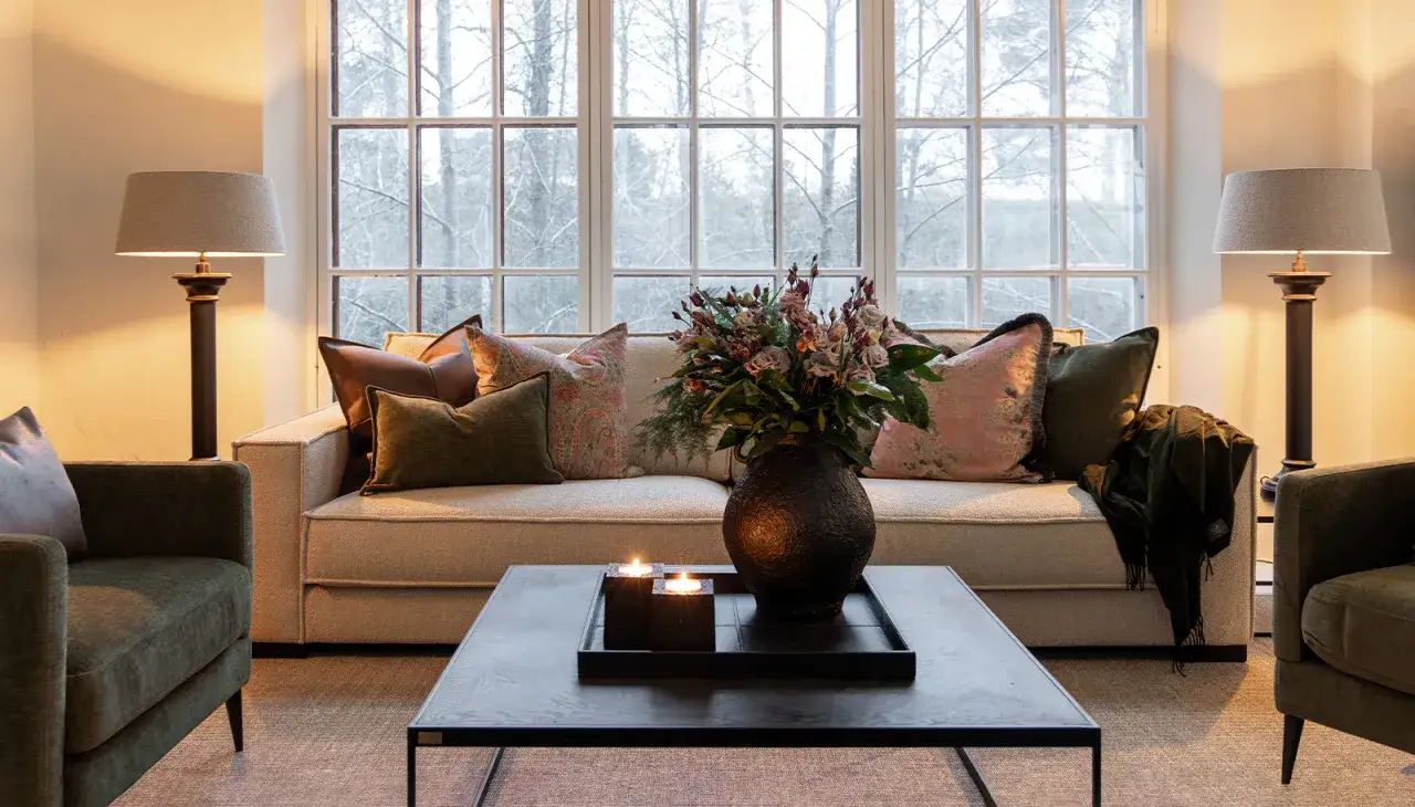 En soffgrupp i modern stil med en beige soffa, gr&ouml;na f&aring;t&ouml;ljer, blommor och ljus p&aring; ett soffbord.