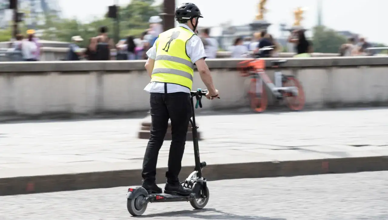 Un homme en trottinette &eacute;lectrique, portant un gilet jaune, roule sur la route. La question 