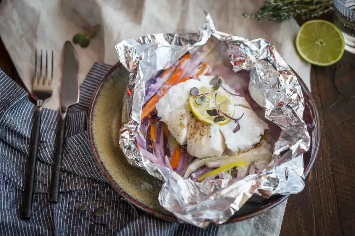 Poisson blanc tendre et légumes colorés, le tout prêt à cuire dans l'aluminium pour un repas sain et savoureux.