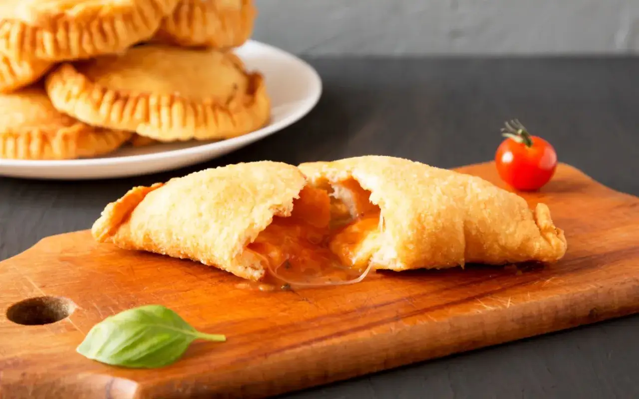 Leckeres Panzerotti-Rezept im Ofen: goldbraun gebackene Teigtaschen mit geschmolzener Füllung, garniert mit Basilikum und Kirschtomate.
