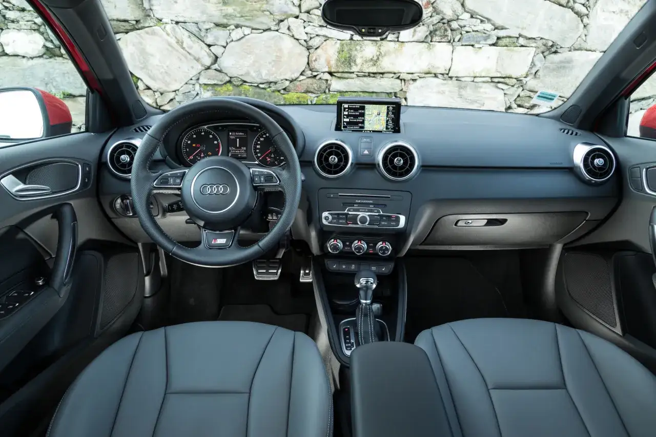 Vue du tableau de bord et des sièges avant de l'Audi A1. Le volant, l'écran multimédia et la console centrale sont visibles.