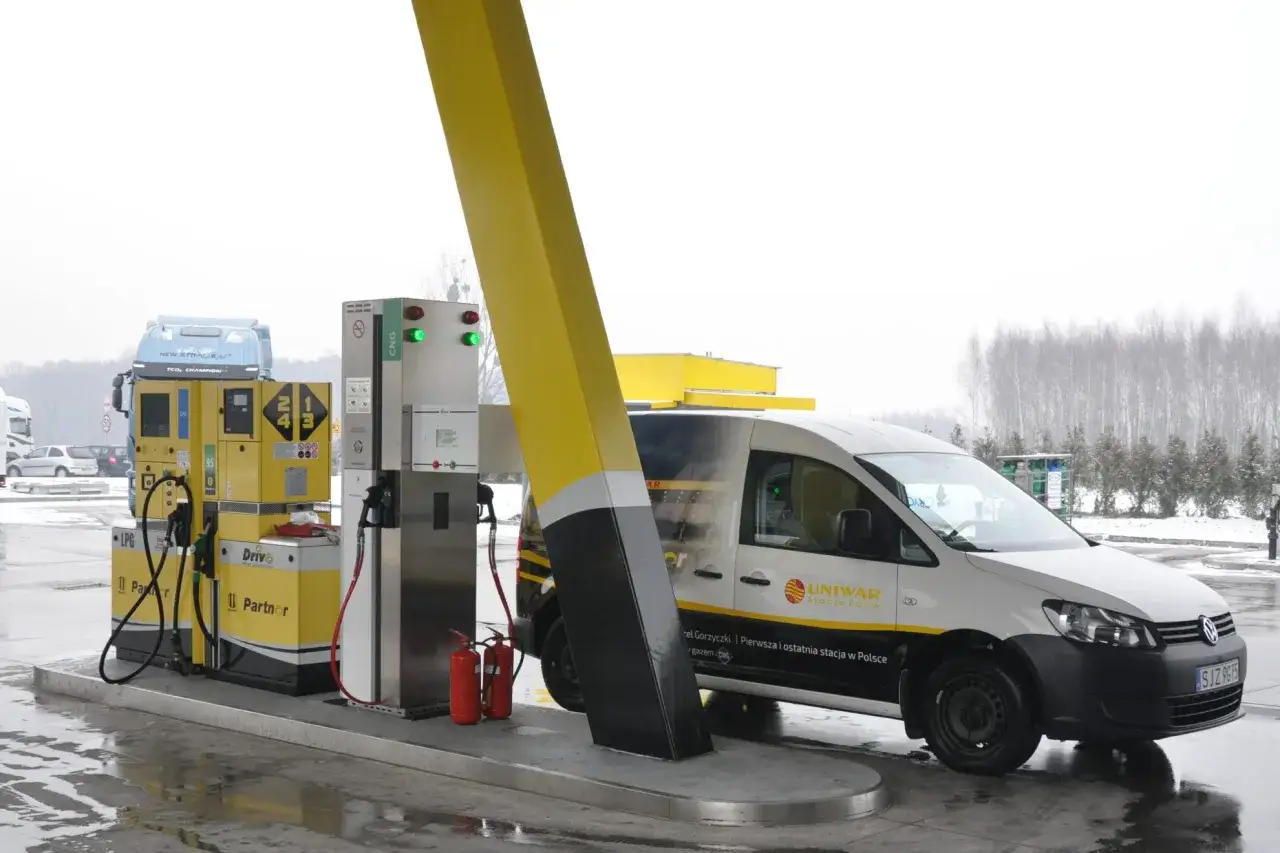 Samochód dostawczy tankuje gaz CNG na stacji paliw. Obok dystrybutory LPG i gaśnice.