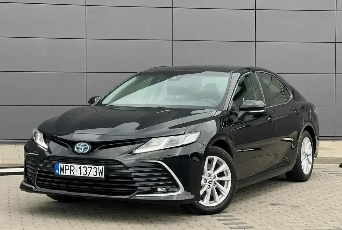 Elegancka, czarna Toyota Camry z polskimi tablicami rejestracyjnymi WPR 1373W stoi przed nowoczesnym budynkiem.