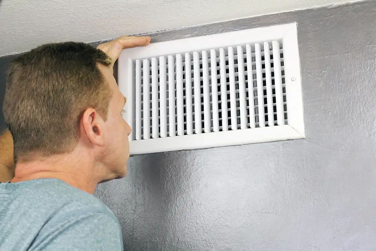 Hombre revisando la salida de aire acondicionado en la pared.