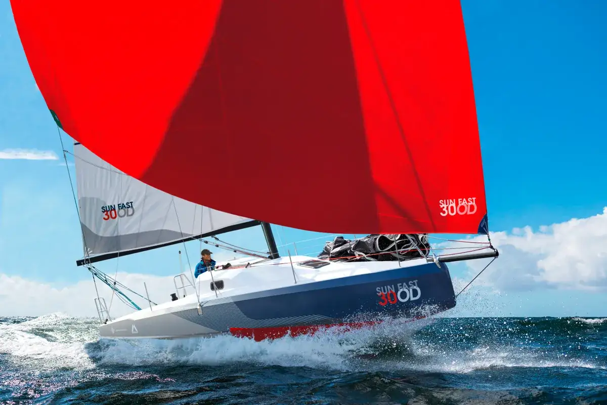 Voile rouge éclatante sur un voilier Sun Fast 30 OD, naviguant à vive allure sur des vagues bleues sous un ciel ensoleillé.