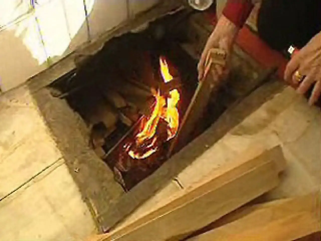 Manos a&ntilde;aden le&ntilde;a a un fuego en un hogar abierto, brindando una gloria de calefacci&oacute;n tradicional.