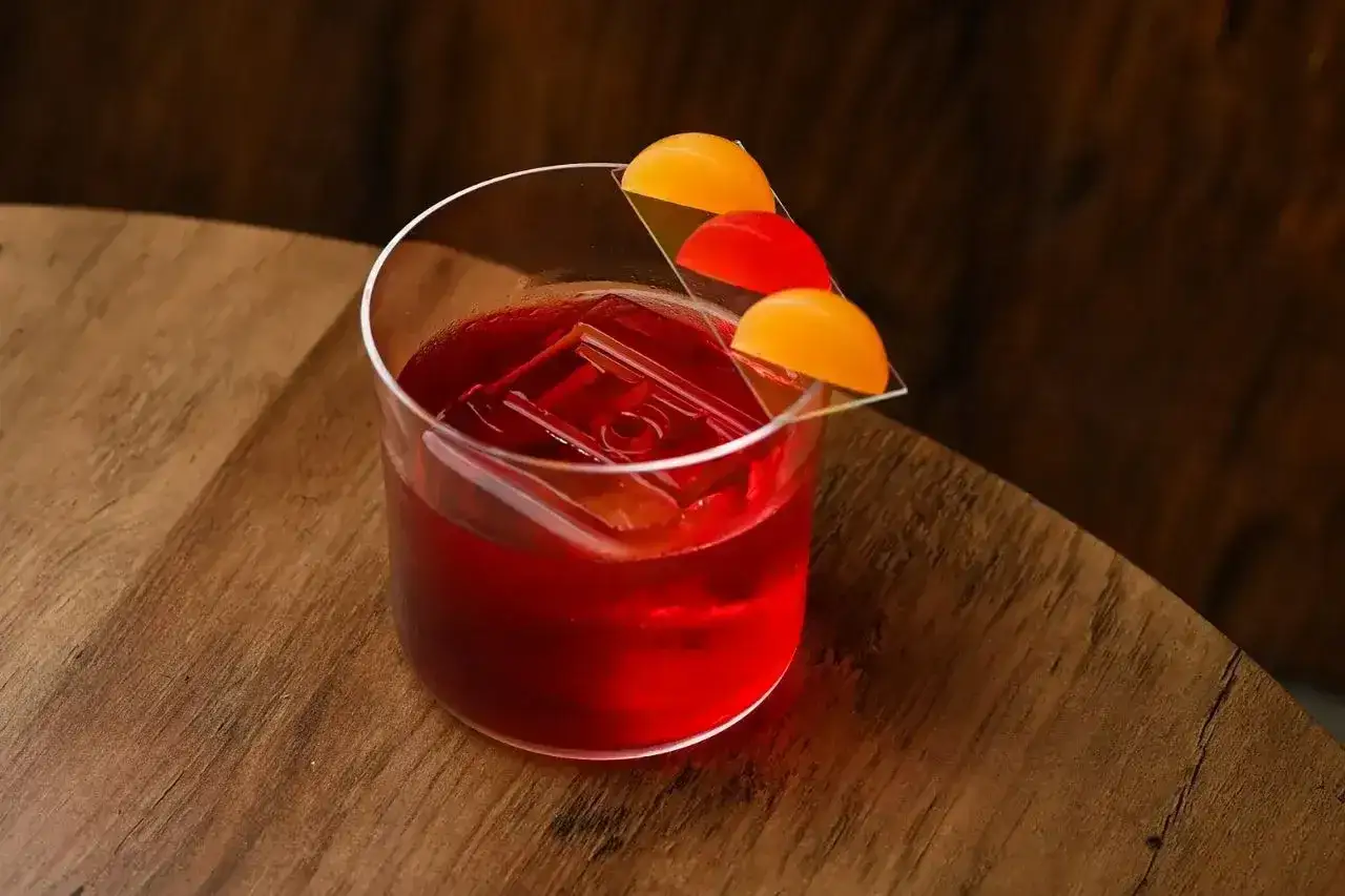 Klasyczny negroni przepis: czerwony koktajl z lodem i pomarańczową dekoracją na drewnianym blacie.