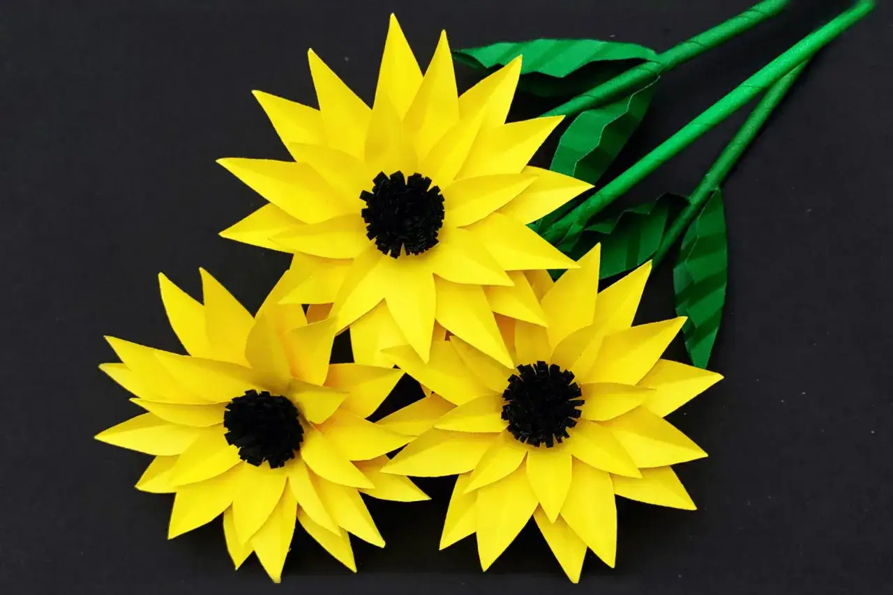 Drei gelbe Papier-Sonnenblumen mit schwarzen Zentren und gr&uuml;nen Stielen, ideal als sonnenblume basteln vorlage.
