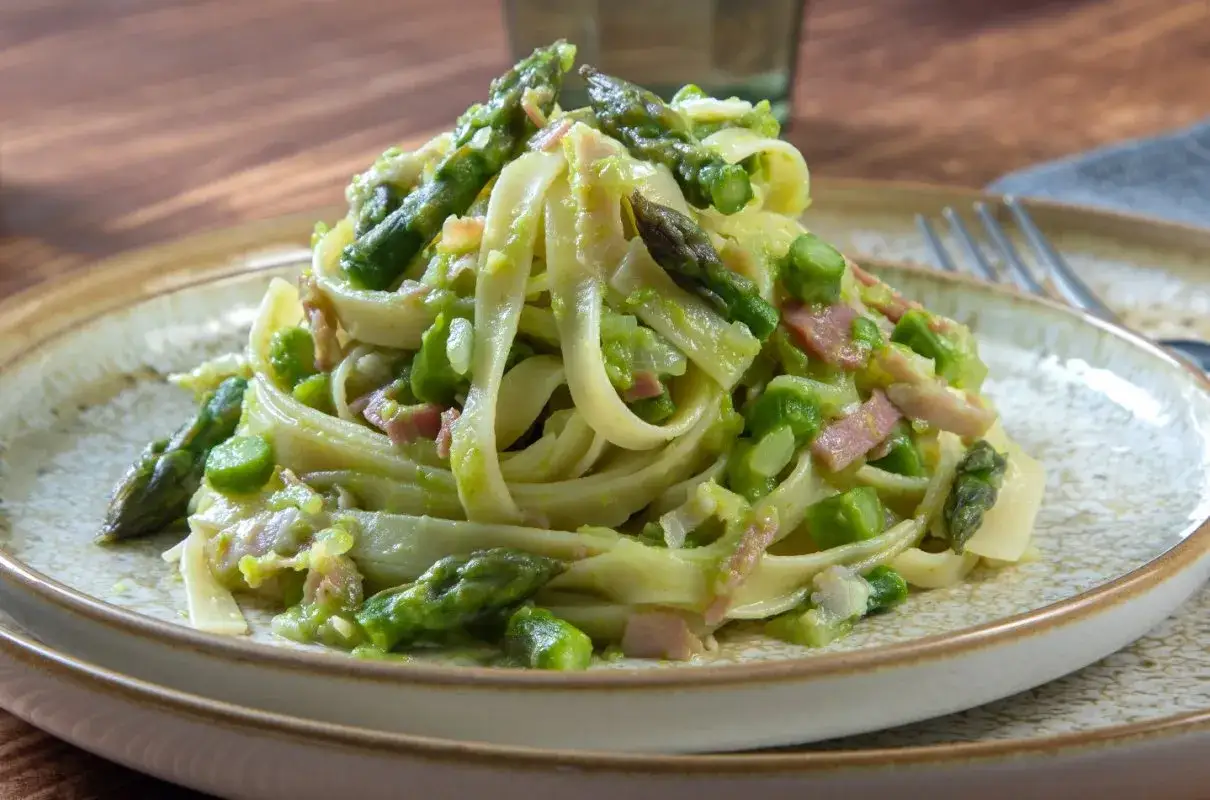Tagliatelle z chrupiącymi szparagami i kawałkami boczku w kremowym sosie. Pyszna carbonara ze szparagami na talerzu.