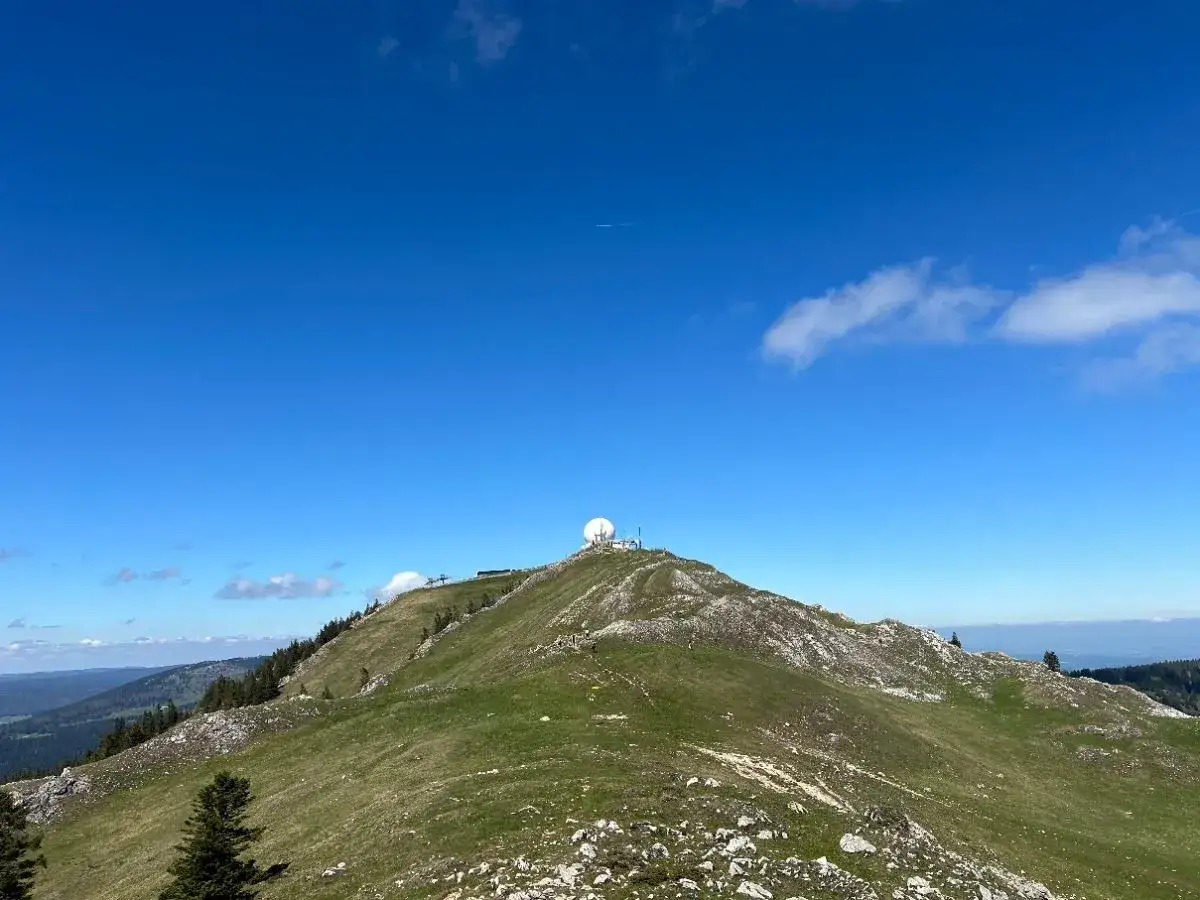 Vue panoramique d'une randonn&eacute;e la d&ocirc;le depuis les dappes. Le sommet rocheux et verdoyant est couronn&eacute; d'une sph&egrave;re blanche.