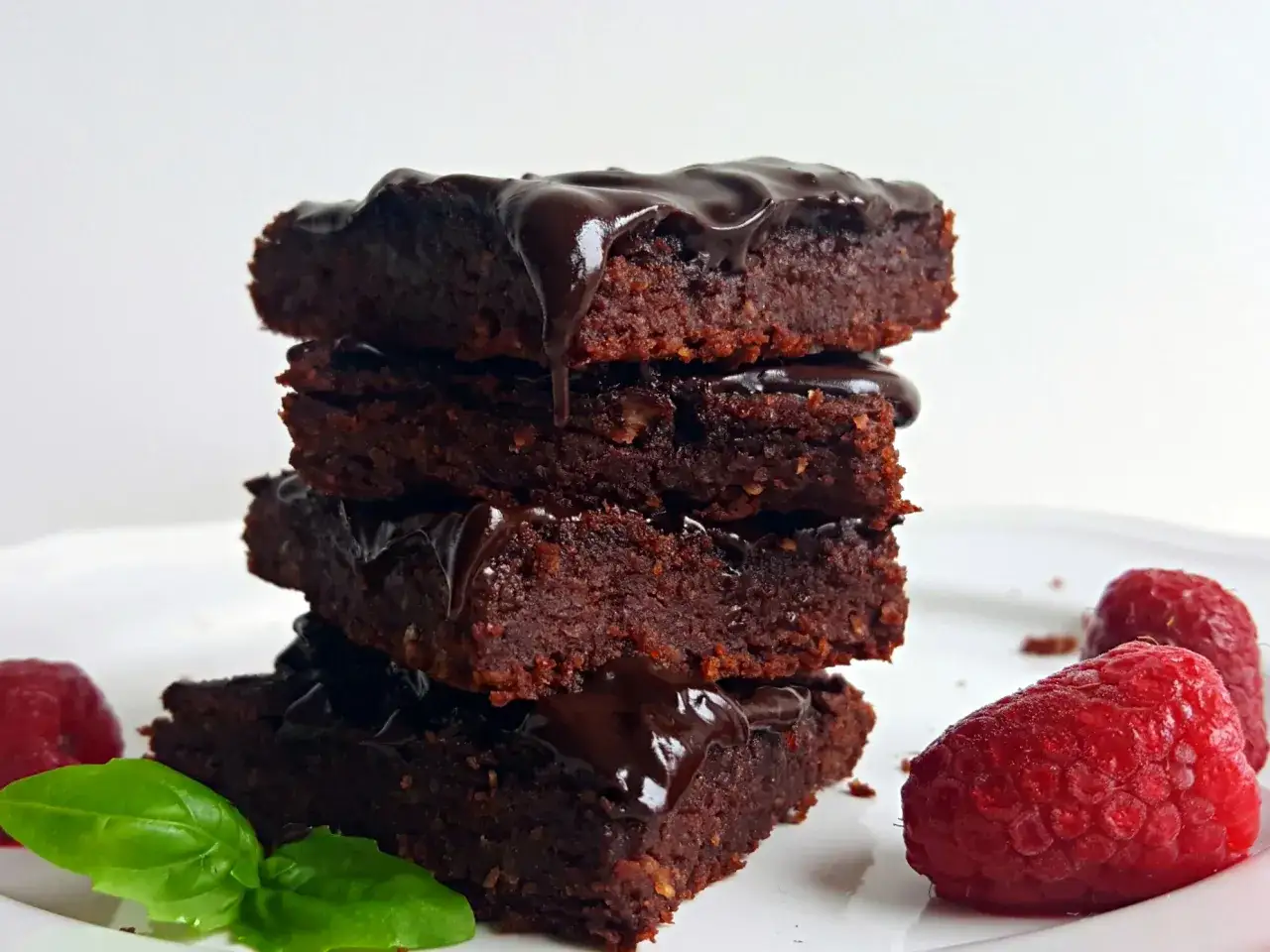 Stos klasycznych brownie z fasoli czy maślanych? Ciemne, wilgotne ciastka z polewą czekoladową, malinami i listkiem bazylii.