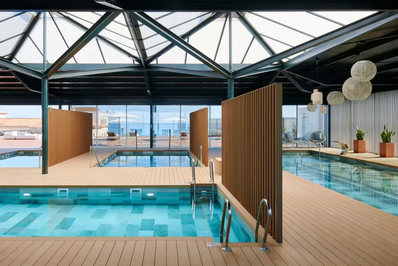 Piscinas interiores con suelo de madera y vistas al mar, perfectas para una experiencia de spa relajante.