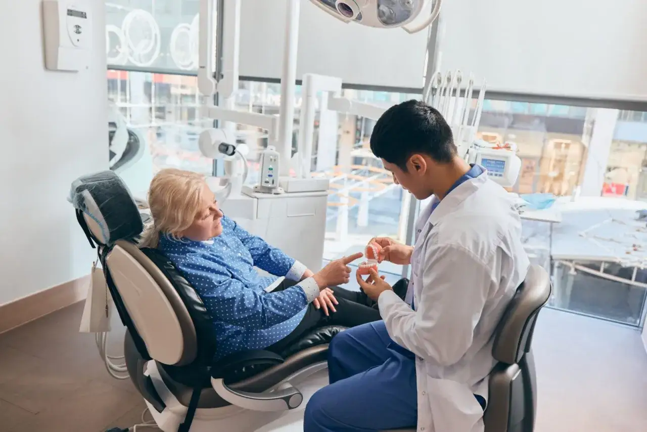 Dentista mostra a paziente un modello di denti, spiegando come rinforzare i denti a cinquant'anni.