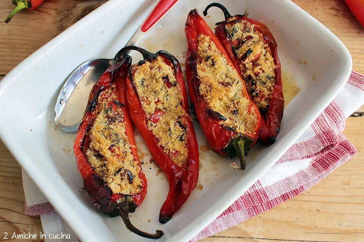 Peperoni cornetti ripieni cotti al forno, dorati e invitanti, serviti in una teglia bianca con un tovagliolo a quadri rossi.