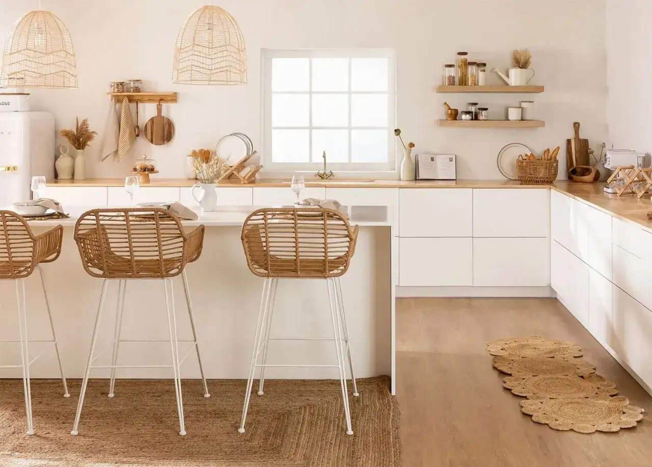 Cuisine lumineuse avec îlot central, tabourets en rotin et vaisselle. Murs et meubles d'un **couleur blanc cassé** apaisante.