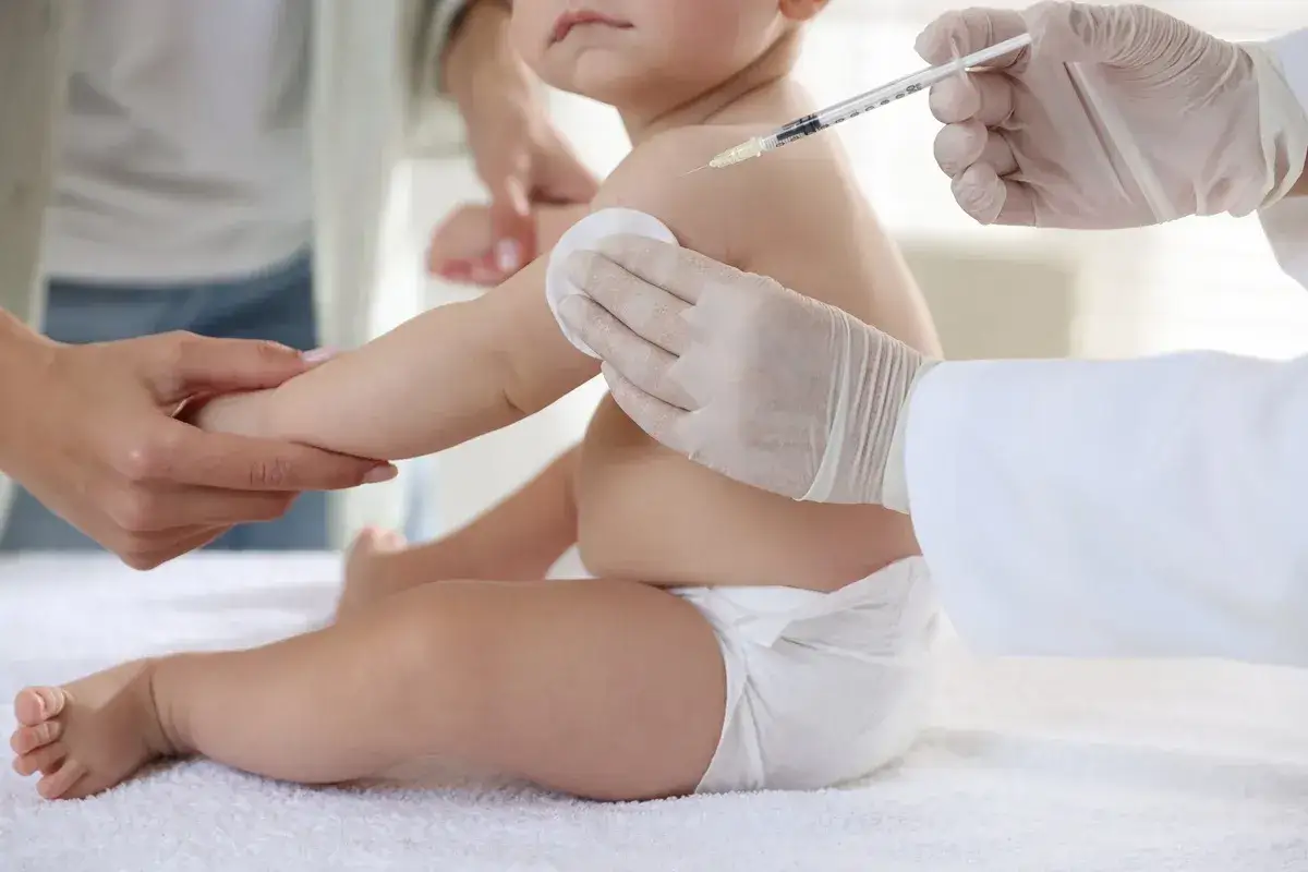 Dziecko otrzymuje szczepienie HPV. Ręka w rękawiczce medycznej podaje zastrzyk, a druga ręka przytrzymuje ramię malucha.