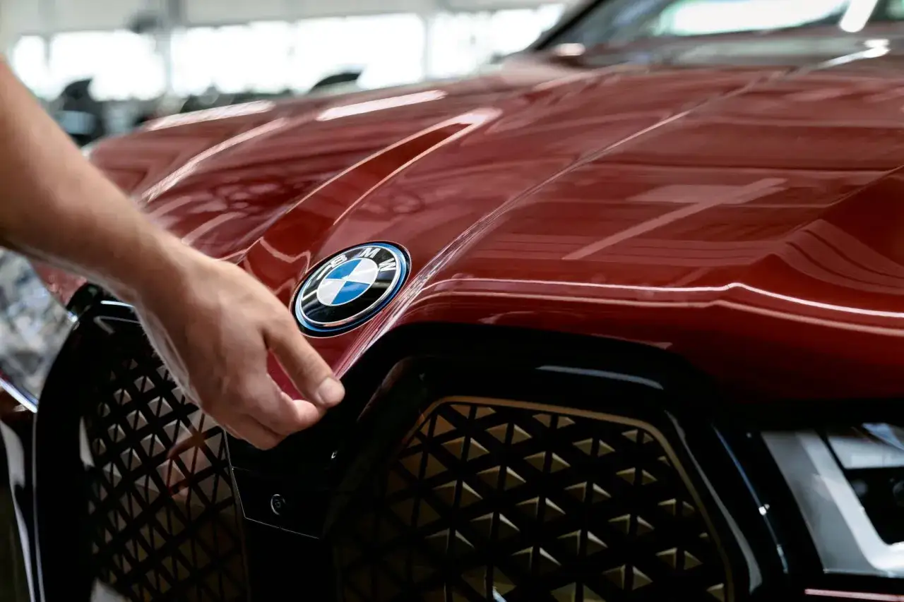 En hand lyfter på motorhuven på en röd BMW. Kanske ett problem med BMW 118d?