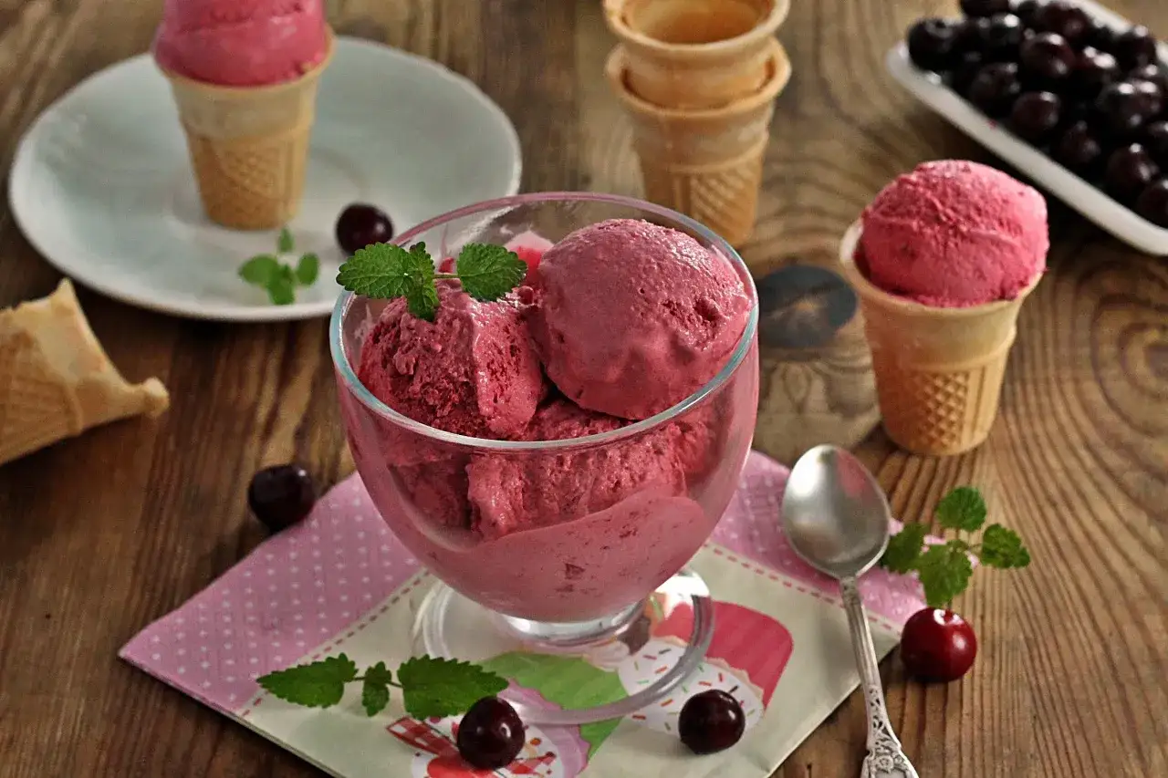 Pyszne lody po francusku o smaku wiśniowym, podane w pucharku i rożku, ozdobione świeżymi wiśniami i miętą.