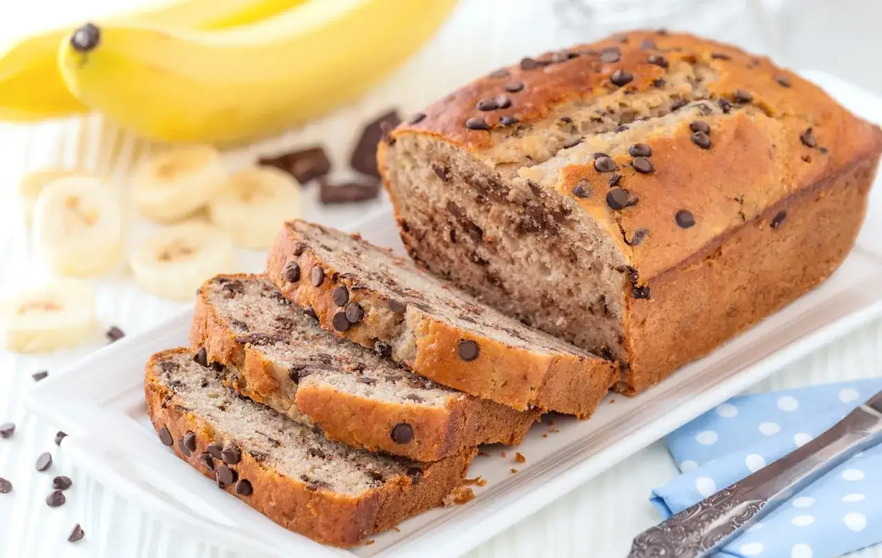 Fetta di plumcake banana e cioccolato, con gocce di cioccolato e banana a fette sullo sfondo.