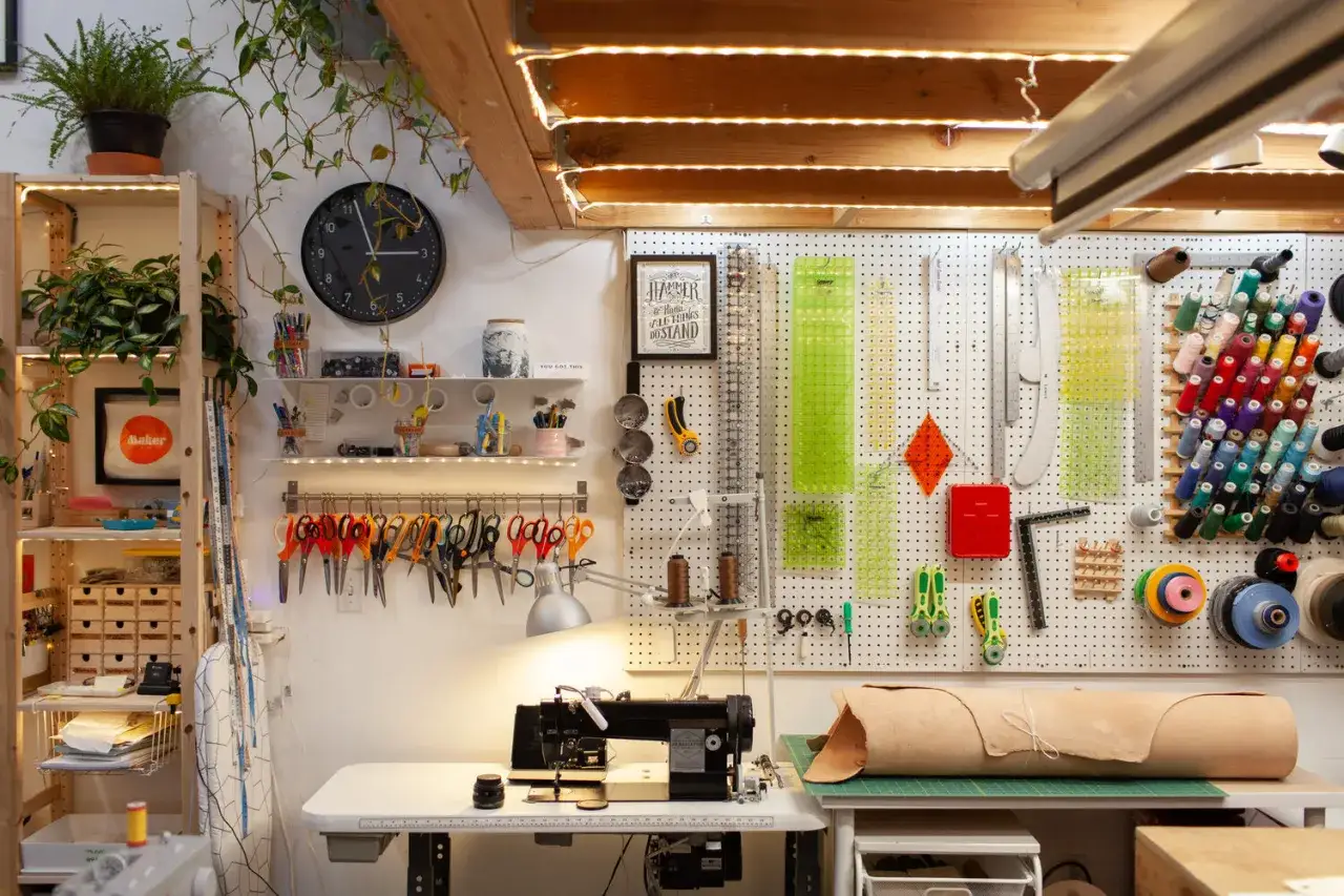A sewing professional's organized workspace, featuring a sewing machine, shelves of supplies, and a pegboard wall displaying rulers, scissors, and colorful thread spools.