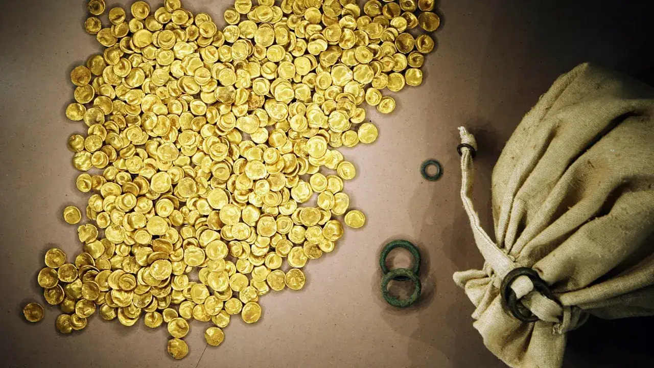 Ein Haufen gl&auml;nzender Goldm&uuml;nzen, Teil des Goldschatzes von Manching, liegt neben einem Leinensack und einigen bronzenen Ringen.