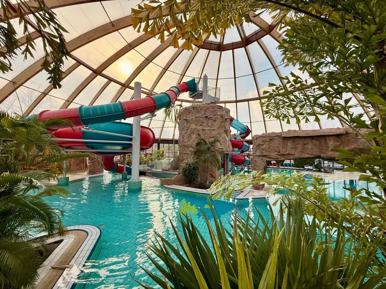 Buntes Rutschenparadies im **Dorsten Freibad** unter einem Glasdach, mit Palmen und Felsen.