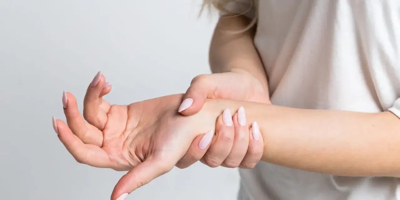 Mano con uñas largas sujetando la muñeca, sintiendo el dolor del túnel carpiano.