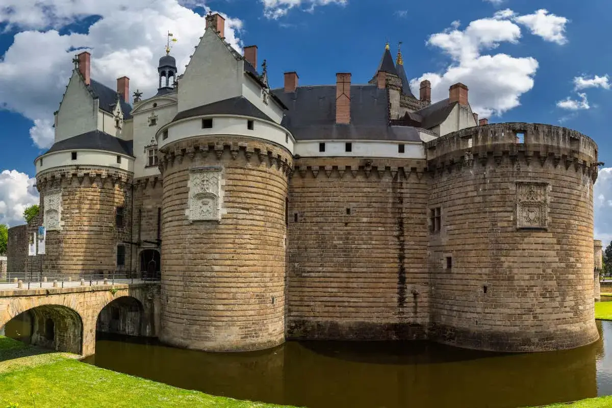 Imponente castillo con foso, un ejemplo de los monumentos de Francia. Torres circulares de piedra y un puente de arco completan la vista.