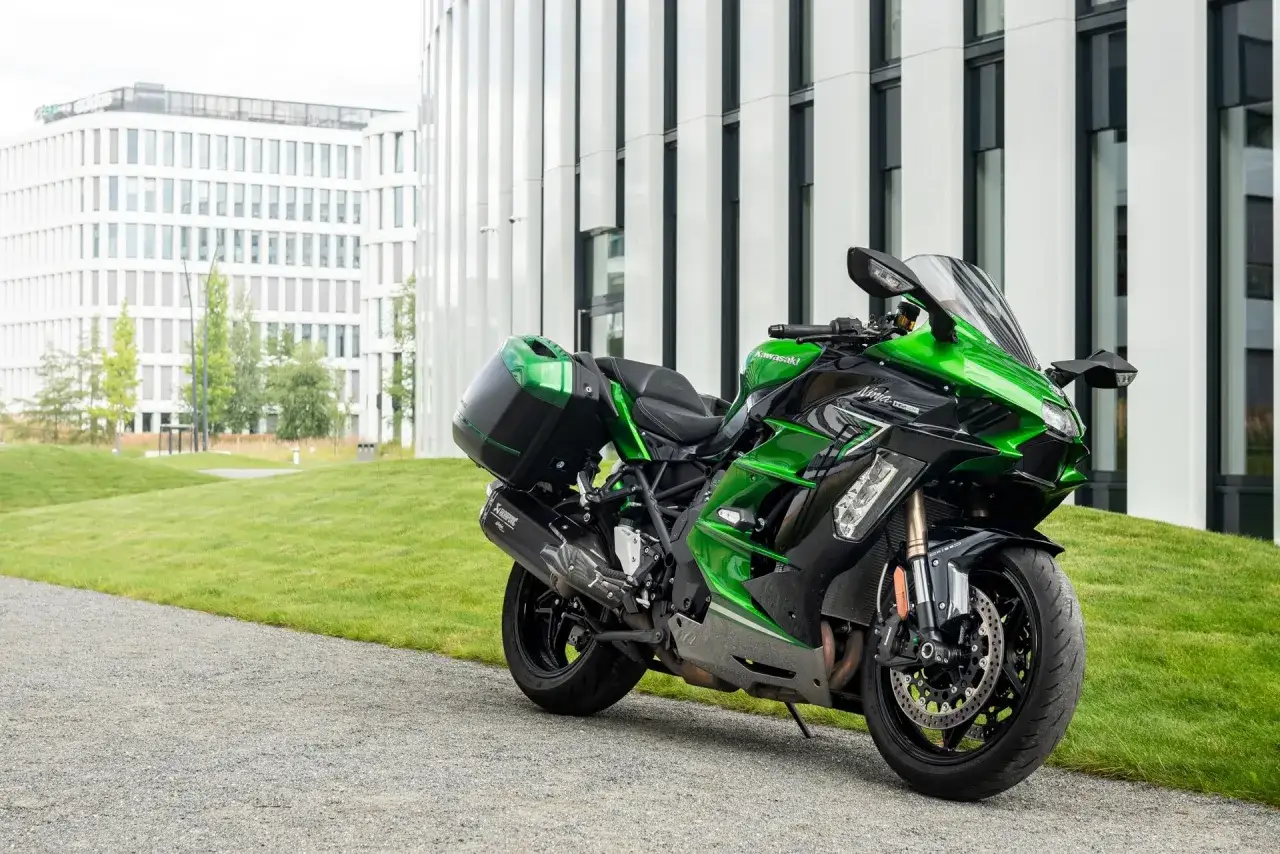 Zielony Kawasaki Ninja H2 z kuframi, gotowy do podróży przed nowoczesnym budynkiem.