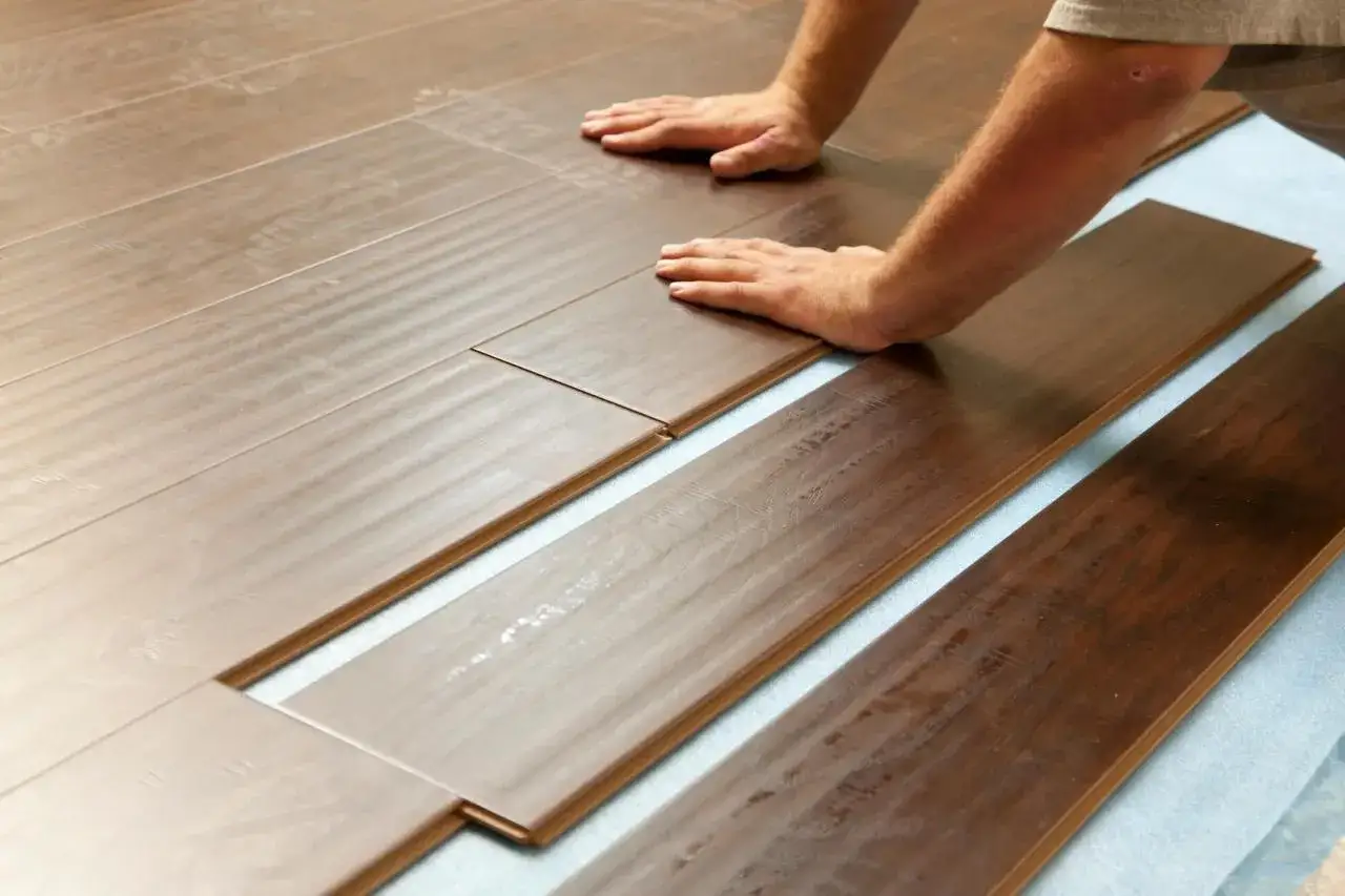 Mani che assemblano assi di parquet scuro, mostrando come si monta il parquet con incastro a click.