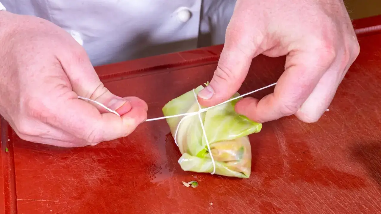 Hände binden Kohlrouladen mit Schnur. Ein Schritt im Kohlrouladen Rezept, um die Füllung sicher zu verpacken.