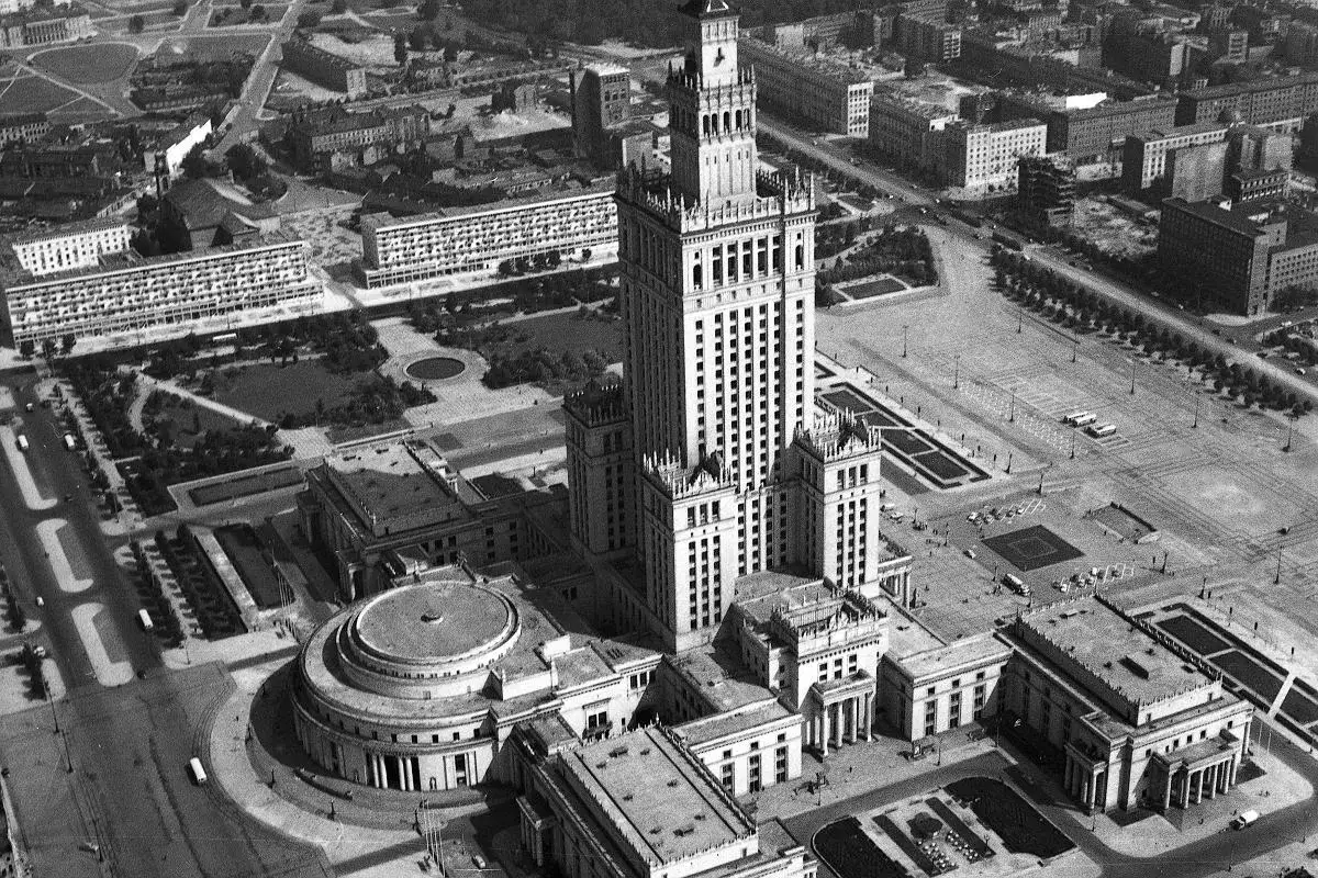 Warszawski Pałac Kultury i Nauki, górujący nad miastem, imponuje swoją wysokością. Widać też otaczające go budynki i plac.