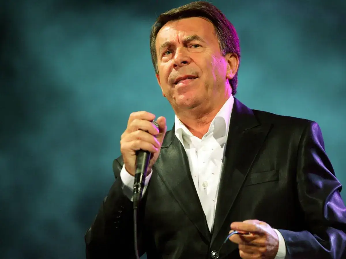 Wojciech Gąssowski, znany z wielu przebojów, śpiewa na scenie. Jego żony pewnie dumne z jego talentu.