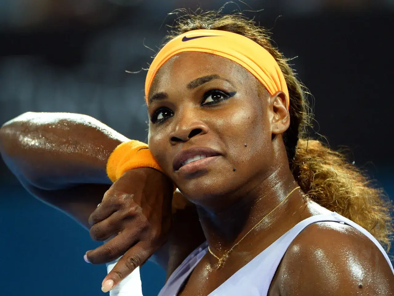 Schweißglänzendes Gesicht einer Tennisspielerin mit Stirnband. Kleine Pickel durch Sport sind auf ihrer Haut sichtbar.
