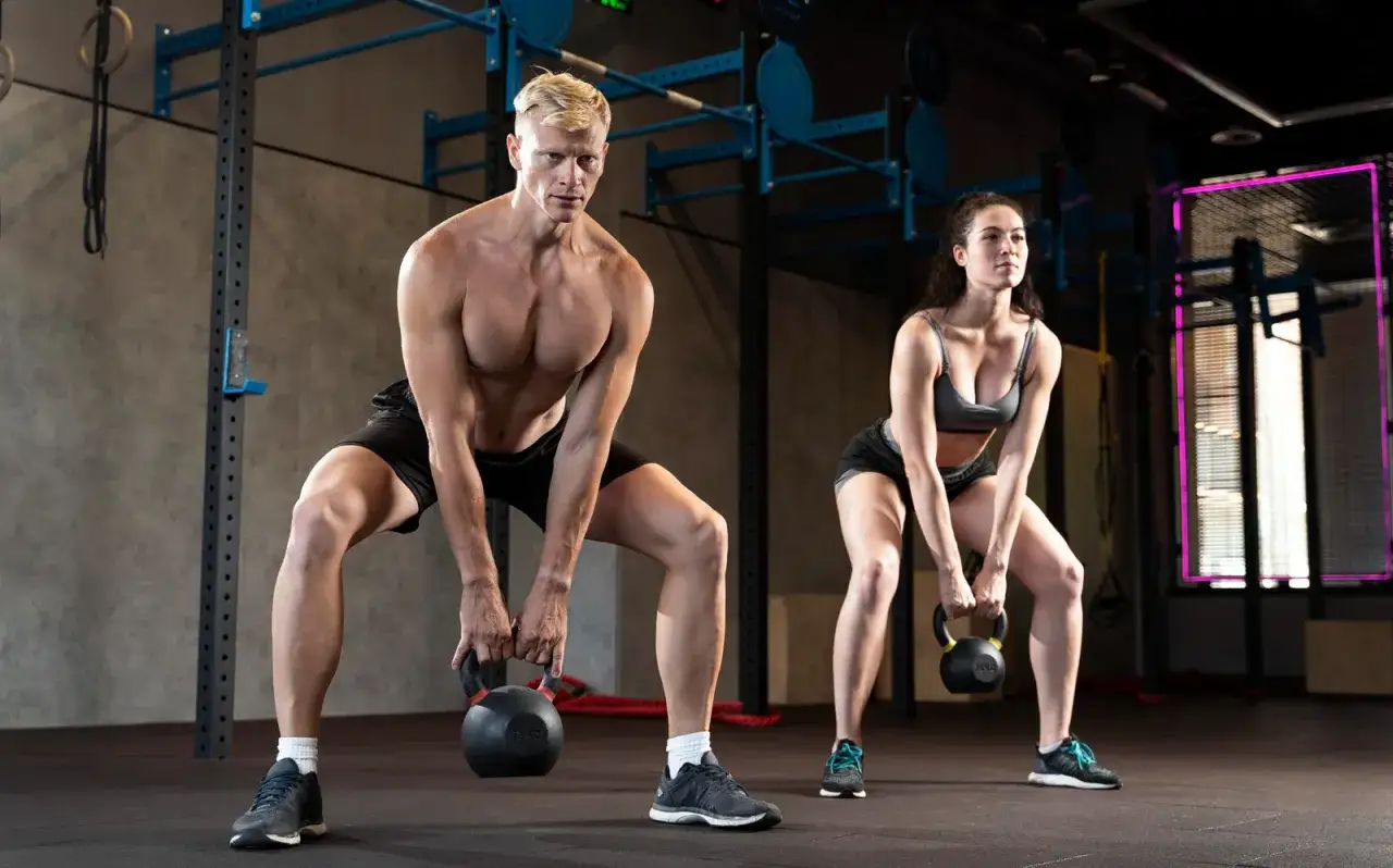 Ein Mann und eine Frau machen Kettlebell-Swings. Sie trainieren im Fitnessstudio, ein Zeichen für **Crossfit gesund** und fit zu bleiben.
