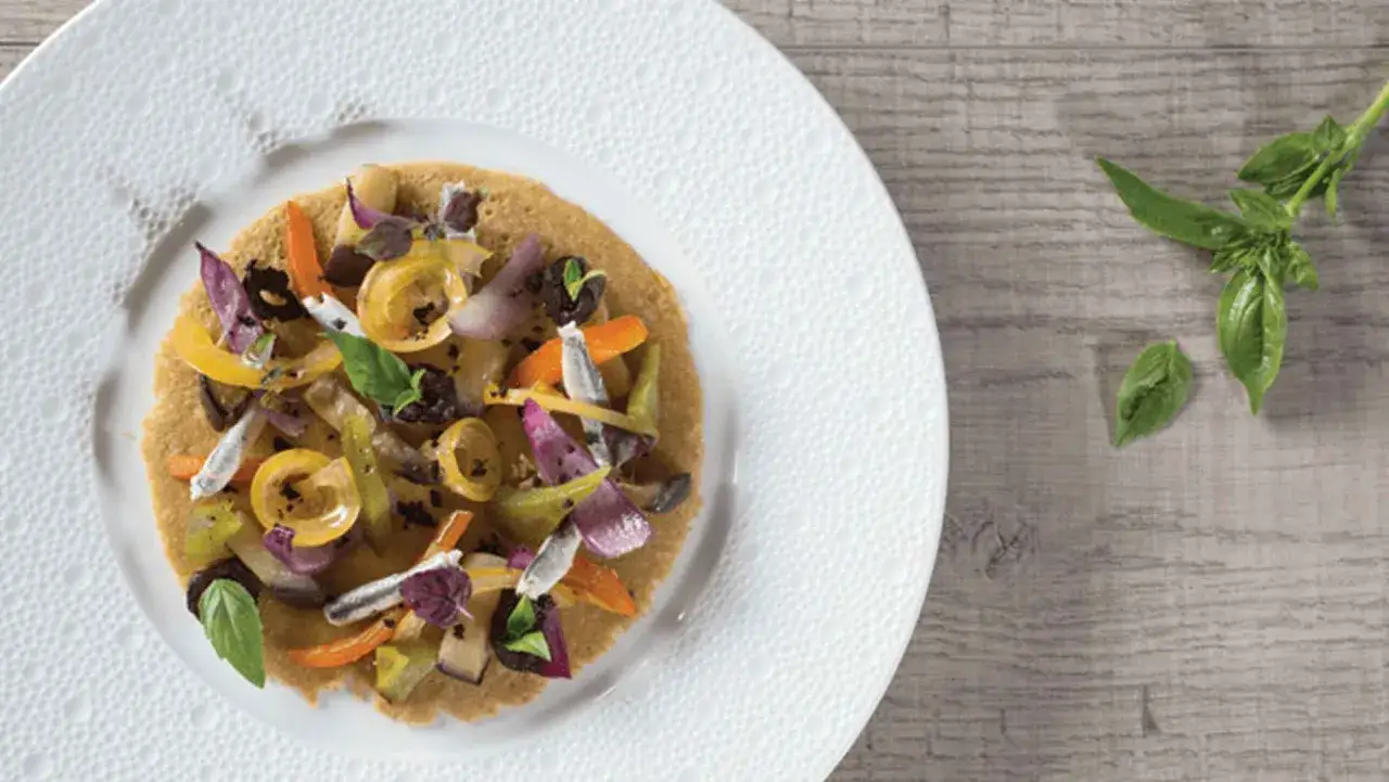 Une socca garnie de l&eacute;gumes color&eacute;s et d'anchois, pr&ecirc;te &agrave; &ecirc;tre d&eacute;gust&eacute;e. Une recette simple et savoureuse.