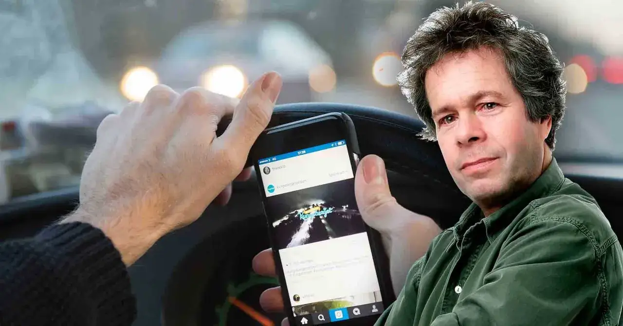 Man håller en telefon i bilen, med ljus från andra bilar i bakgrunden.