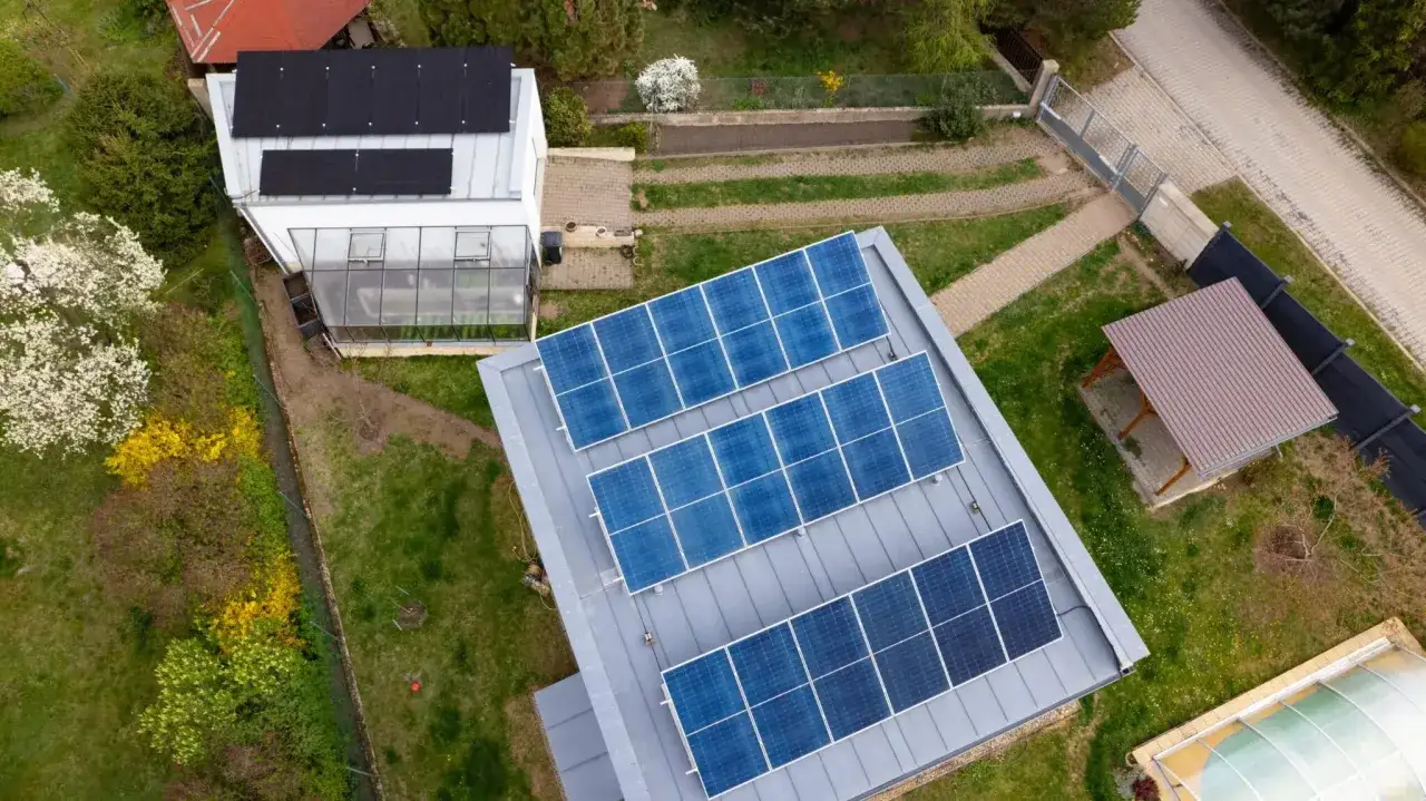 Ein **selbstversorger autarkes Haus** mit Solaranlagen auf dem Dach und einem Gewächshaus. Grüne Wiesen und blühende Bäume umgeben das Anwesen.