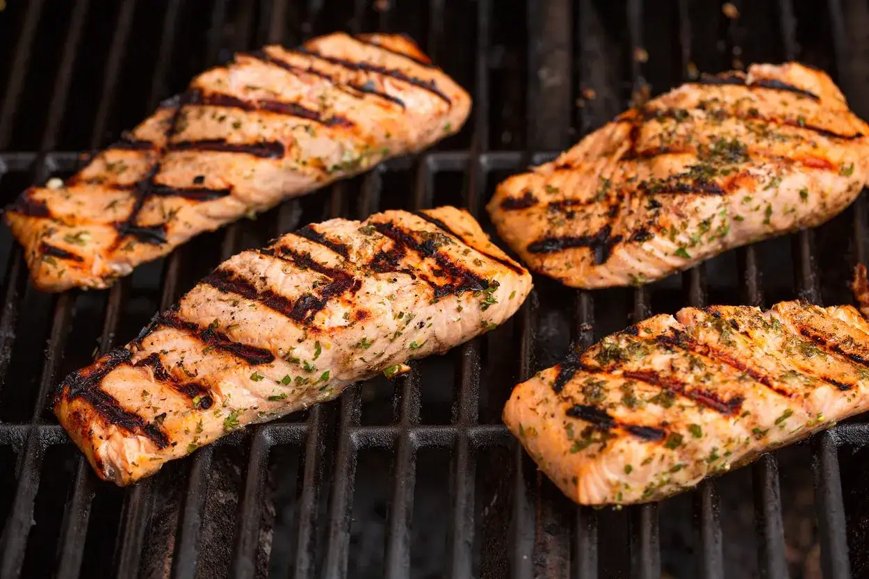 Vier saftige Lachsfilets mit Grillstreifen und Kräutern, perfekt mariniert, brutzeln auf dem Rost.