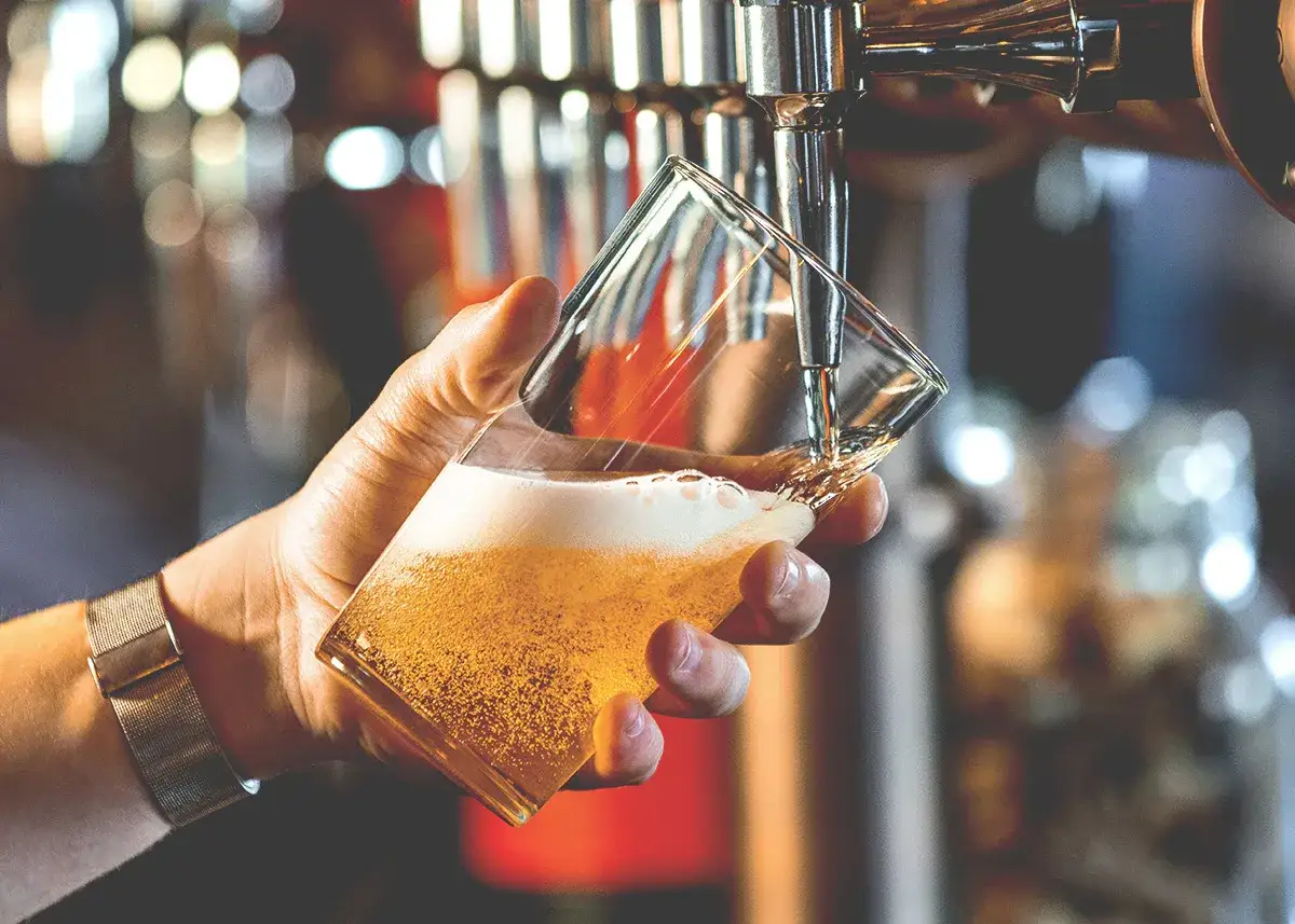 Mano che versa birra dorata in un bicchiere, creando una ricca schiuma birra.