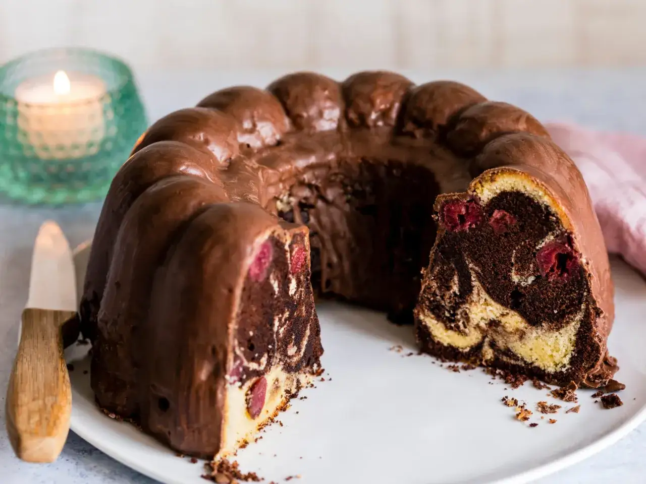 Ein saftiger Marmorkuchen mit Kirschen, &uuml;berzogen mit Schokoladenglasur, wartet auf einem Teller.