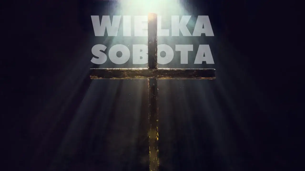 Promienie światła przebijają się przez mrok, oświetlając drewniany krzyż i napis 