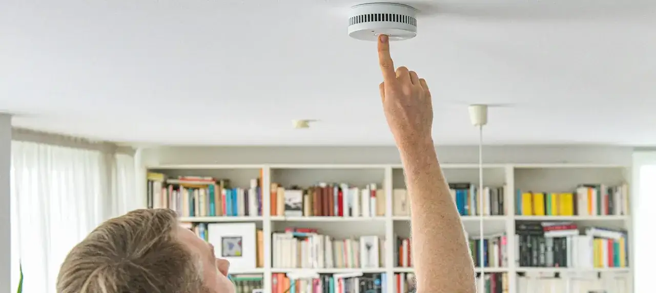 Mann drückt auf den Rauchmelder an der Decke, um ihn zu testen. Sicherheit geht vor!
