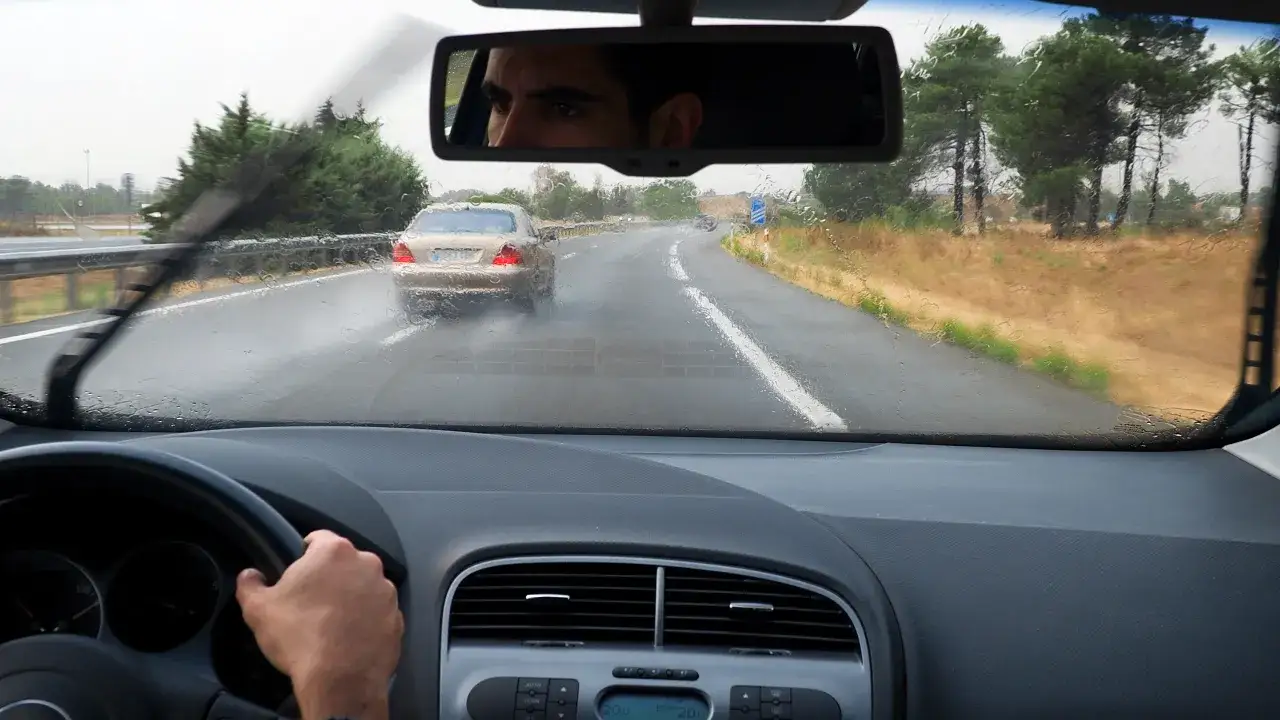 Widok z kabiny samochodu podczas deszczu. Wycieraczki pracują, a przed nami jedzie inny pojazd. To sytuacja, gdzie liczy się bezpieczne wymijanie.