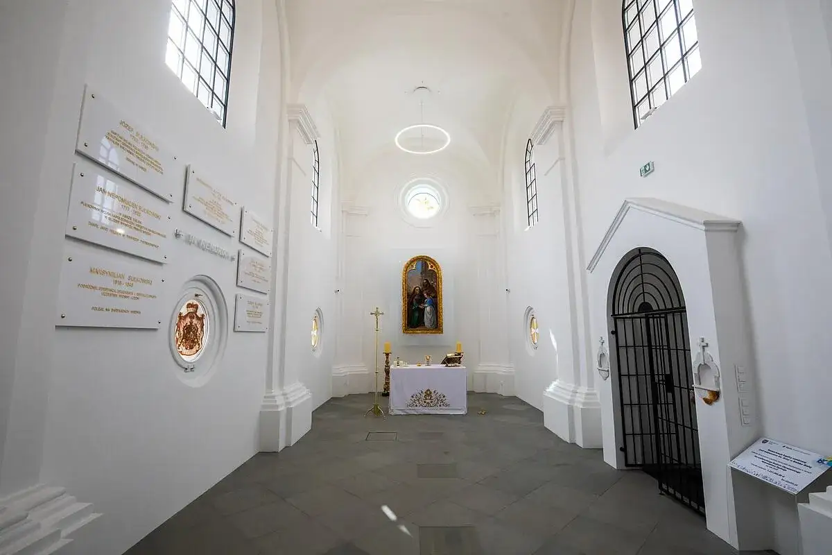 Wnętrze kaplicy św. Anny w Karpaczu. Białe ściany, ołtarz z obrazem, tablice pamiątkowe i kraty.