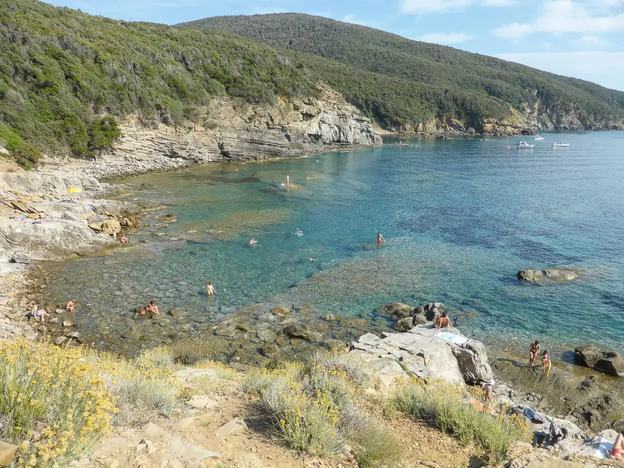 Baia con acque cristalline e scogli, ideale per chi cerca cosa vedere a Baratti. Gente che nuota e si rilassa al sole.