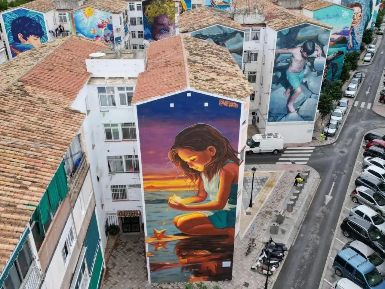 El **soho viertel Malaga** se llena de arte con murales gigantes en edificios. Una ni&ntilde;a mira una estrella en un atardecer pintado.