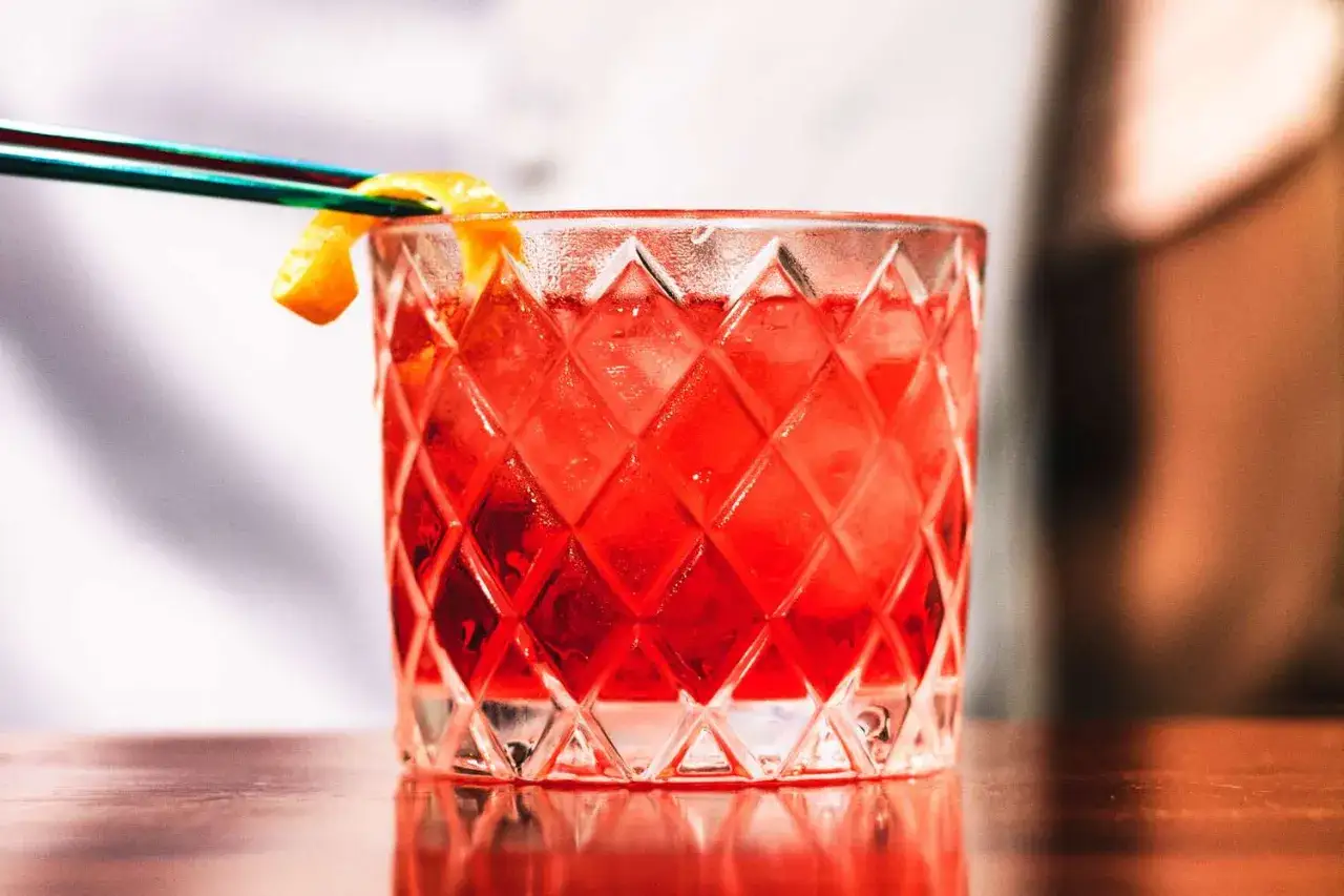 Ein leuchtend roter Cocktail mit Eis und Orangenzeste, serviert in einem Glas mit Rautenmuster. Das ist die Frage: was ist Campari?