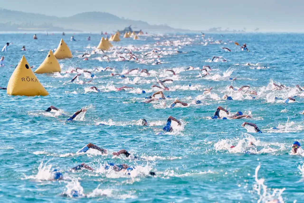 Schwimmer kämpfen sich durch das Meer, ein Teil der Ironman Vorbereitung. Gelbe Bojen markieren den Kurs.